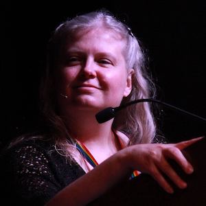 Photo of Stephanie Zvan at podium in high-contrast lighting.